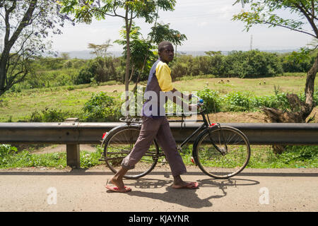 A young African man walking with a bicycle by the roadside, Kenya, East Africa Stock Photo