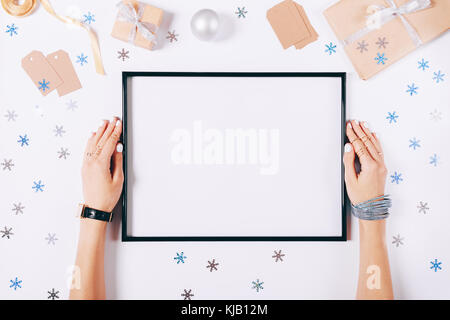 Beautiful female hands are holding the empty frame on a white background among the Christmas decorations, top view Stock Photo
