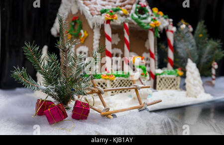 Sprig of Christmas tree with small gifts near gingerbread house on dark background. Mockup for seasonal offers and holiday post card Stock Photo