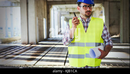 Male architect with blueprints using walkie-talkie Stock Photo