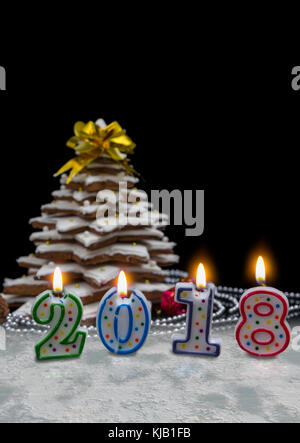 Candles in the form of 2018 new year near homemade gingerbread Christmas tree with decorations on dark background. Mockup for seasonal offers and holi Stock Photo