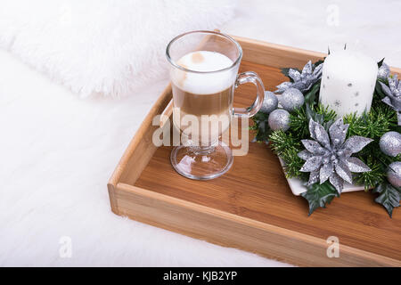 A cappuccino drink and Christmas decoration with candle, fir branch and silver balls on white furry carpet. Stock Photo