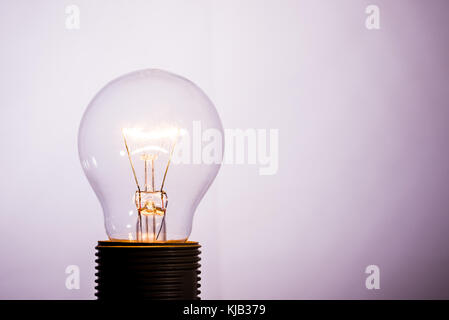 Horizontal photo with single glass bulb. The bulb is switched on and the wire inside is hot and is shining. The background is light with shadows in co Stock Photo