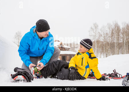 Caucasian father adjusting snowshoe for son Stock Photo