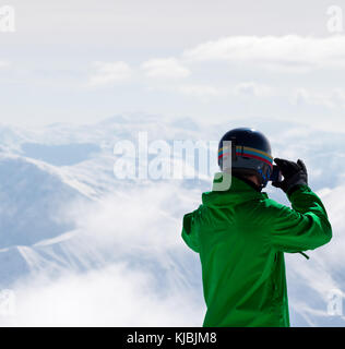 Snowboarder makes photo on camera and snowy mountain in fog at background. Caucasus Mountains in winter, Georgia, region Gudauri. Stock Photo