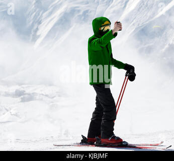 Skier makes selfie on camera phone and snowy winter mountain in fog at background. Caucasus Mountains, Georgia, region Gudauri. Stock Photo