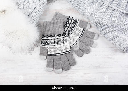 Winter knitted gloves, fur hat and pullover on white wooden background. Set of grey knitted clothes. Stock Photo