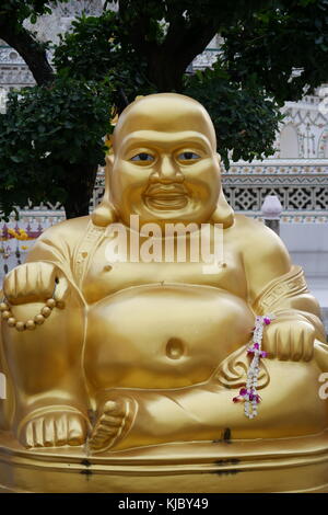 A Laughing Buddha golden statue, a Chinese deity known as Budai, Hotei or Pu-Tai, sits in front of Wat Arun temple in Bangkok. Stock Photo