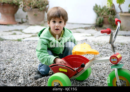 Boy Putting Small Stones in Tricycle Stock Photo