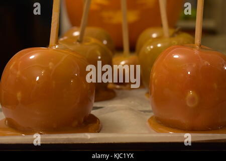 Freshly made caramel apples made with melted caramel sitting in front of a carved pumpkin on Halloween. Stock Photo