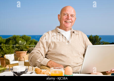 Man on Patio Eating Breakfast, Using Laptop Computer Stock Photo