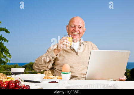 Man on Patio Eating Breakfast, Using Laptop Computer Stock Photo