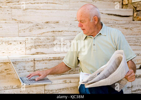 Man Reading Newspaper and Using Laptop Computer Stock Photo