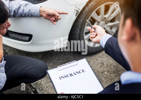 Insurance agent writing on clipboard while examining car after accident claim being assessed and processed Stock Photo