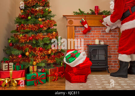 Santa Claus delivering gift wrapped presents under the tree on Christmas Eve with a sack full of toys for good girls and boys. Stock Photo