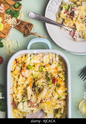 Pasta casserole with romanesco cabbage and ham in creamy sauce,  served in plate with fork on kitchen table with ingredients, top view, close up.  Ita Stock Photo