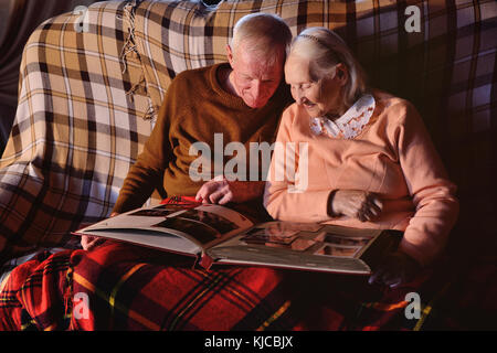 An elderly couple is considering a family photo album wrapped up in a plaid Stock Photo