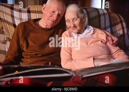 An elderly couple is considering a family photo album wrapped up in a plaid Stock Photo