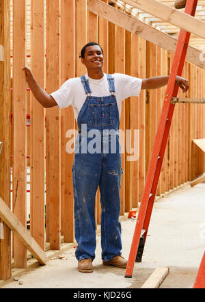 Portrait of smiling mixed race man leaning on ladder at construction site Stock Photo