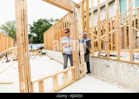 Smiling volunteers holding framed wall at construction site Stock Photo