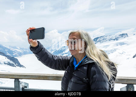 Caucasian woman posing for cell phone selfie near snowy mountains Stock Photo