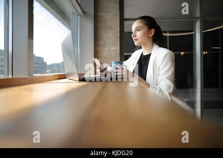Caucasian woman drinking coffee and texting on cell phone Stock Photo