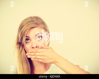 Saying bad things, shocking news concept. Ashamed young blonde woman having hand on her mouth Stock Photo