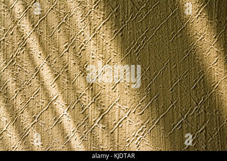 Texture from embossed stucco plaster lit by sunlight with playful shadows. Close-up of beige wall in retro style with pattern from diagonal scratches. Stock Photo