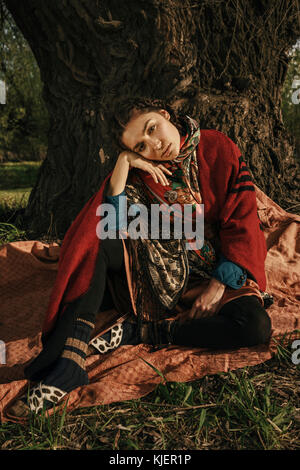 Caucasian woman wearing traditional clothing sitting near tree Stock Photo