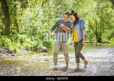 Couple holding hands wading in river Stock Photo