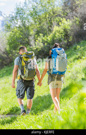 Couple carrying backpacks hiking on hill Stock Photo