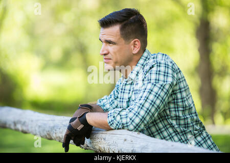 Man wearing gloves leaning on wooden fence Stock Photo