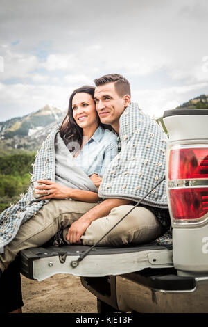 Couple wrapped in blanket sitting on bed of pick-up truck Stock Photo