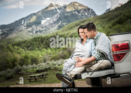 Couple wrapped in blanket sitting on bed of pick-up truck Stock Photo