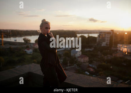 Pensive Caucasian woman standing on roof at sunset Stock Photo