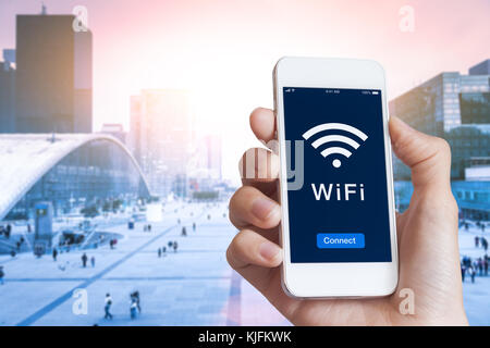 Business person connecting to WiFi hotspot on smartphone screen in financial district to access wireless internet with blurred cityscape in background Stock Photo