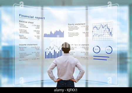 Businessman analyzing financial report data of the company operations (balance sheet, income statement) on virtual computer screen with business chart Stock Photo