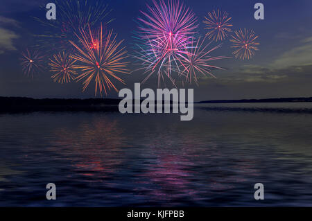 Colorful fireworks in the sky above the river with reflections on the water surface. Can be used as wallpaper. Stock Photo