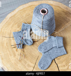 Cone of grey fluffy cashmere, knitting needles and newborn baby socks on a round wooden table. Stock Photo