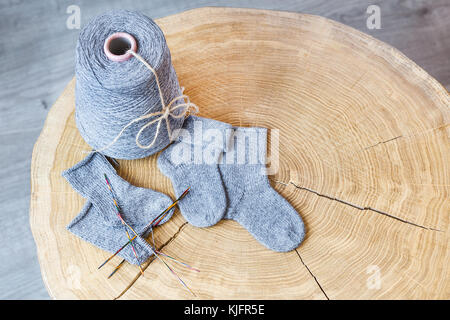 Cone of grey fluffy cashmere, knitting needles and newborn baby socks on a round wooden table. Stock Photo