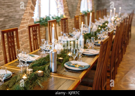 christmas, decor, catering concept. adorable tableware for celebrating, lots of shining white plates, glowing wine glasses, burning candles and fresh spruce branches Stock Photo