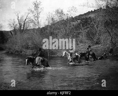 Photograph of a group of Native American women fording (crossing a river at a shallow place) on horseback, titled 'Apache women fording', by Edward S Curtis, 1903. From the New York Public Library. Stock Photo