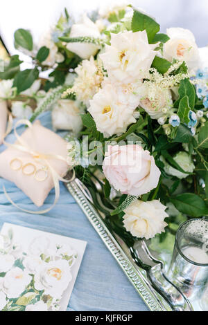 marriage, sentiment, proposal concept. wonderful bridal bouquet of elegant creamy and pink roses decorated with small blue flowers placed on the silver shining tray nearby with pillows for rings Stock Photo