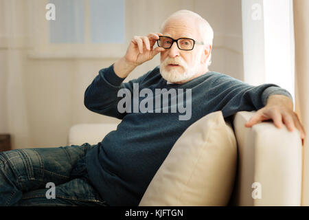 Concentrated bearded man touching his glasses Stock Photo