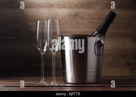 Image of two empty wine glasses, bottle of champagne in bucket on wooden background Stock Photo