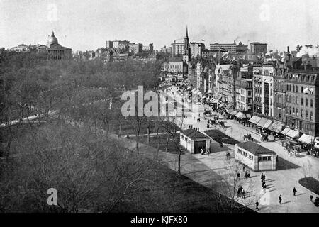 A photograph taken from a elevated position of the subway station entrances and exits along Tremont Street next to Boston Common, the grass and walkways of the park can be seen through the trees which are barren of leaves, many city buildings can be seen along the street and in the background, people are walking along the sidewalks and horsedrawn carriages are travling along the street, development of Boston Common started in 1634 making it the oldest public city park in the United States, Boston, Massachusetts, 1905. Stock Photo