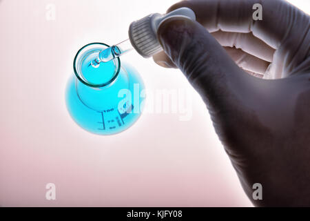 Laboratory worker hand with dropper and glass chemical containers on glass table in the laboratory. Top view Stock Photo