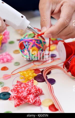 closeup of a young man making a handmade christmas ball using a hot glue gun with strings and buttons of different colors, and a pile of different hab Stock Photo