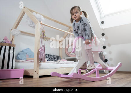 Toddler girl rocking on rocking horse in nursery Stock Photo