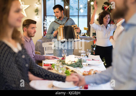 Young man playing accordion for family at Christmas Stock Photo